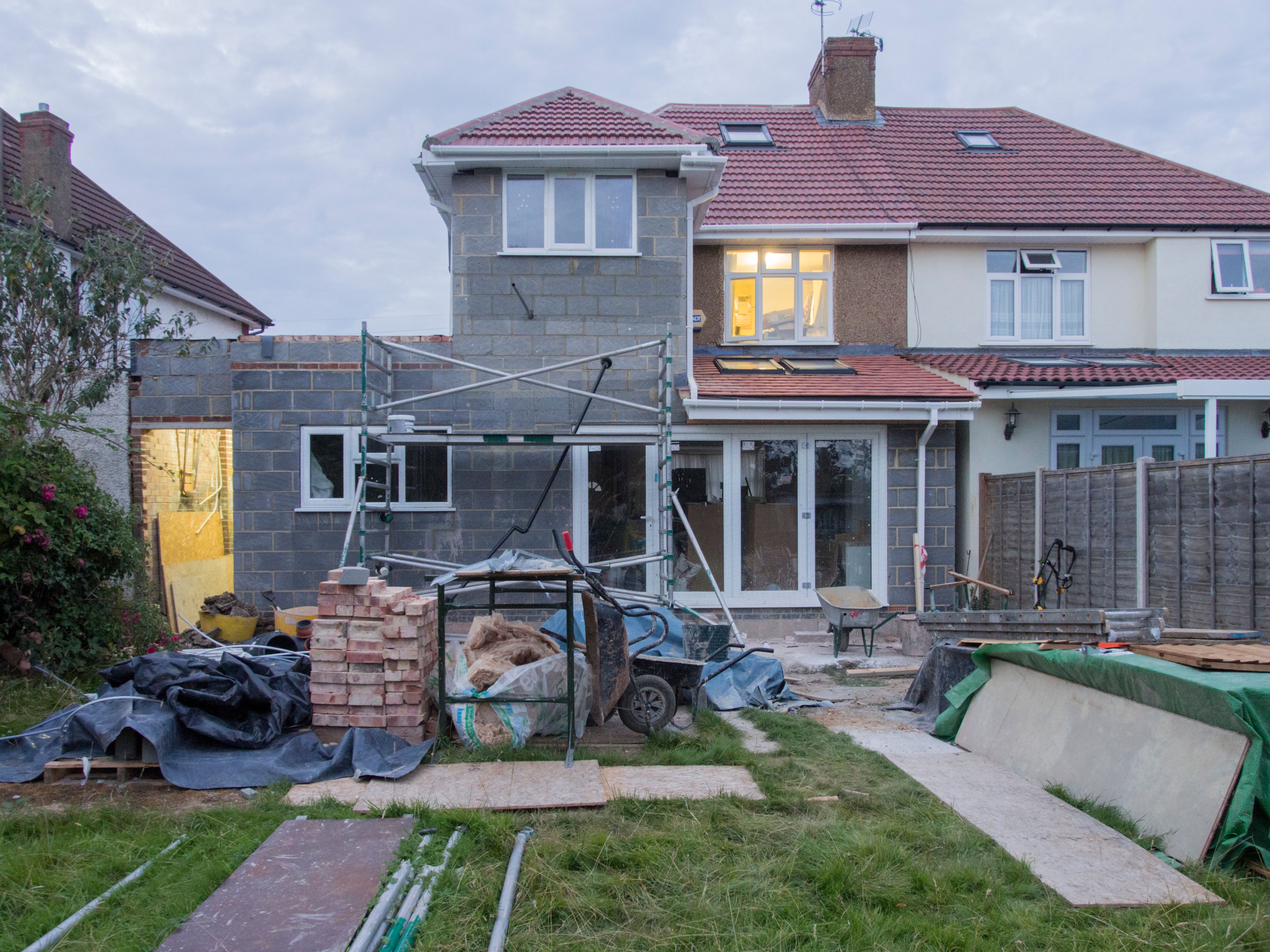 A suburban house undergoing major renovation with scaffolding and building materials outside.
